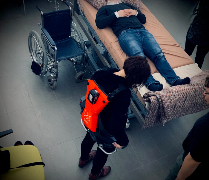 Patient liegt auf dem Bett. Pflegerin hat ein Exoskelet an