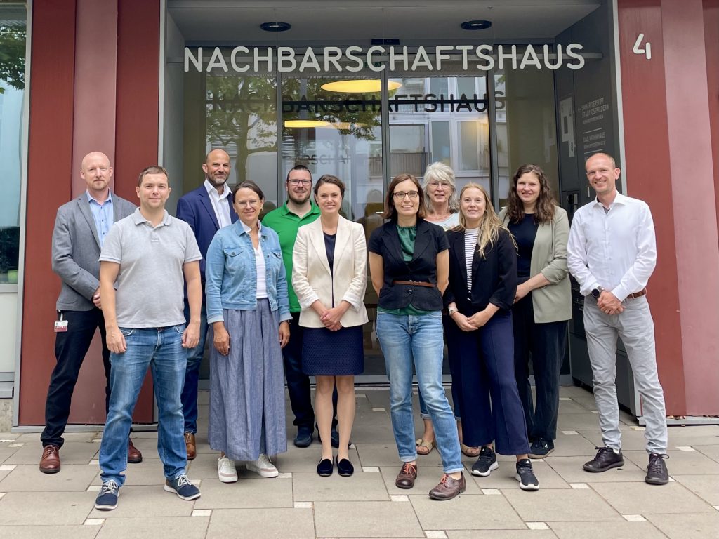 Gruppenbild mit 11 Menschen. Sie stehen vor einem Haus mit: Nachbarschaftshaus